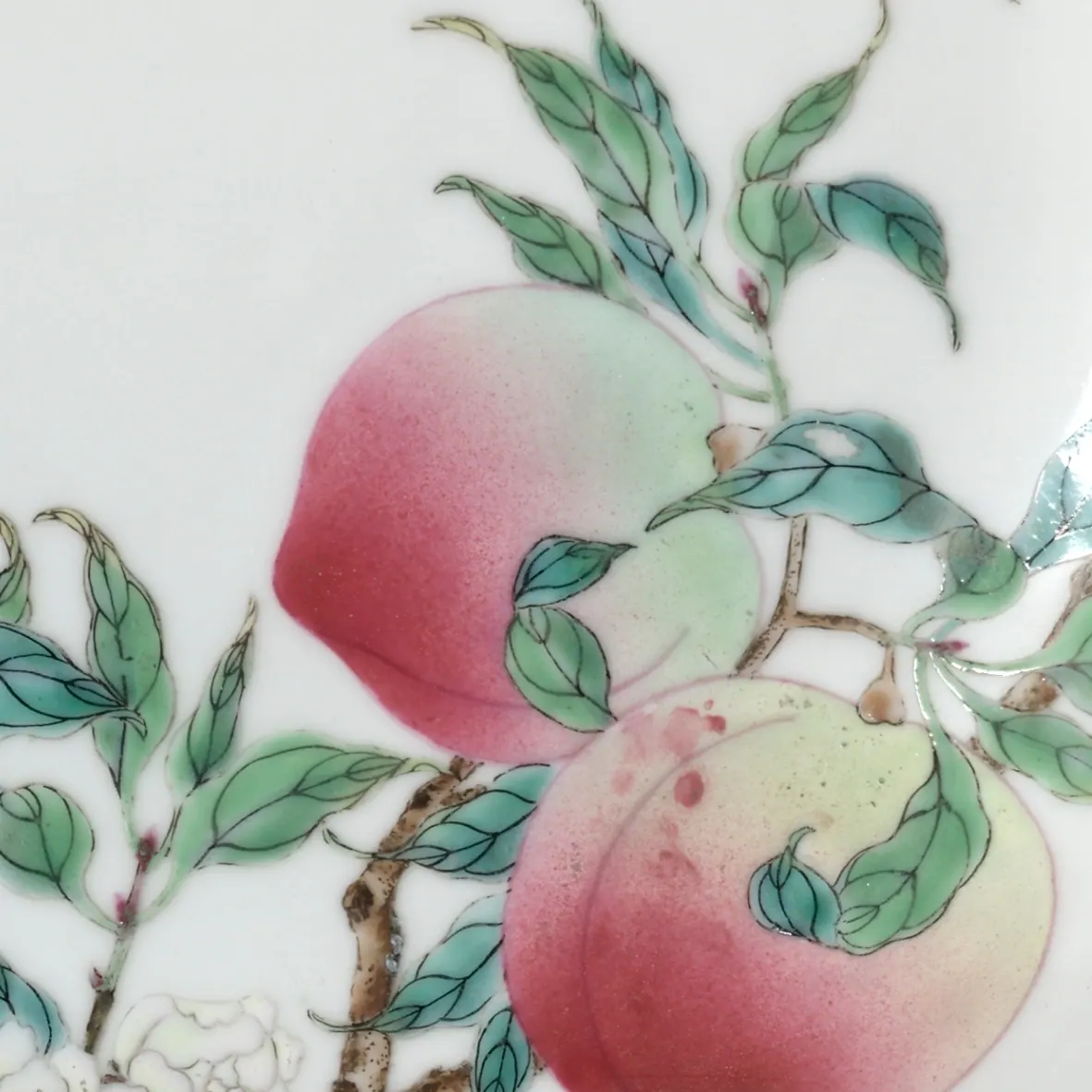 Detail of a Yongzheng famille rose dish, about 8 cm across: two peaches in opaque pink enamel shaded through white to pale green, among green leaves