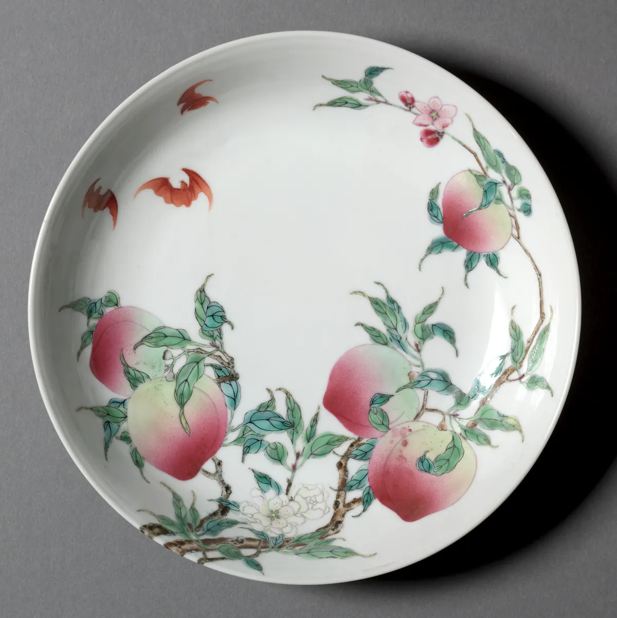 Yongzheng porcelain dish painted in famille rose enamels with a peach branch bearing pink-shaded fruit and blossom, and red bats flying across the white ground