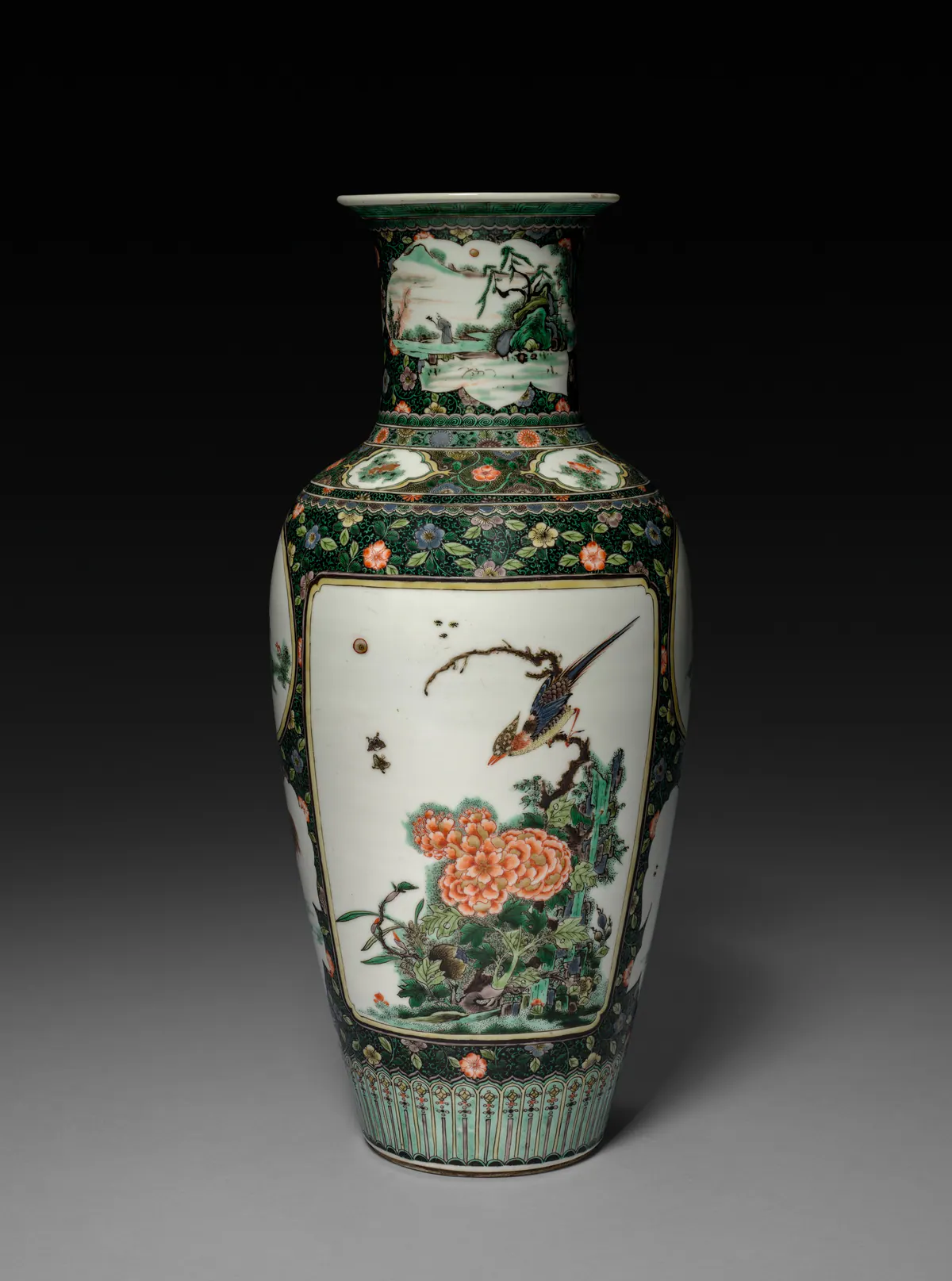 Kangxi porcelain baluster vase painted in famille verte enamels, with a long-tailed bird on a branch above peonies and rockwork in a white panel framed by dense black and green floral borders