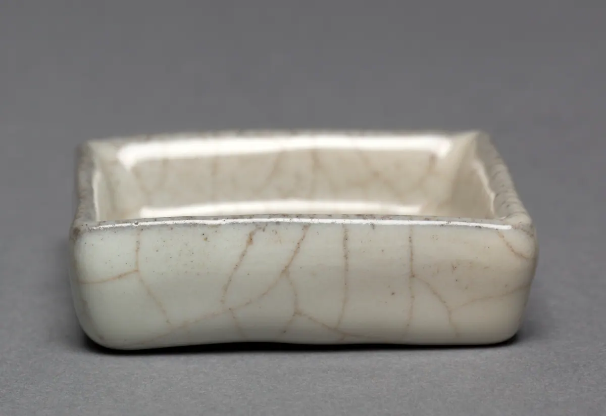 A small square Guan ware brush washer with softly rounded corners, its thick, pale grey glaze crossed by a bold network of brown crackle lines.