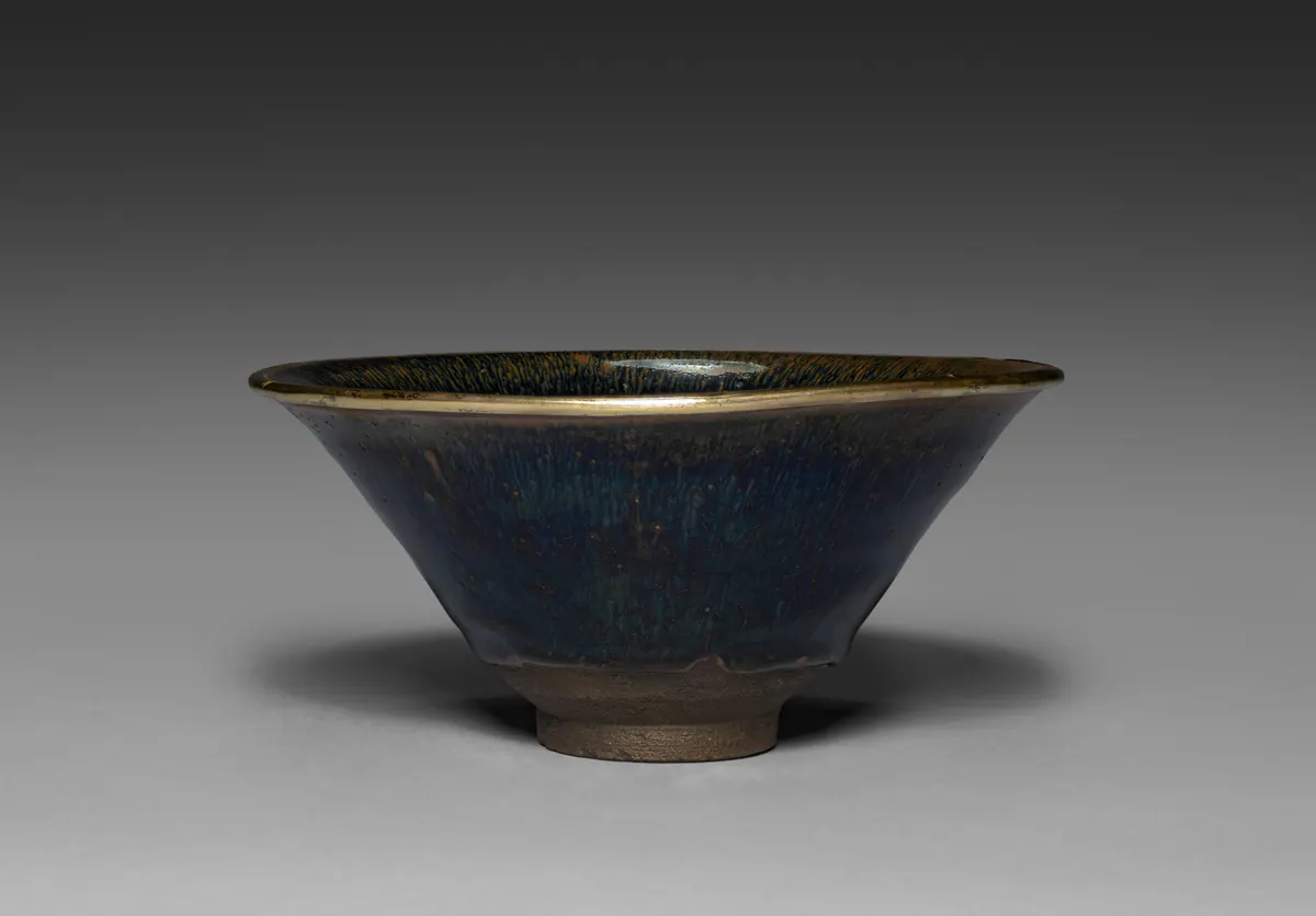 A conical Jian ware tea bowl with a black glaze streaked with fine brown hare's fur lines, a metal-bound rim and a dark unglazed foot.