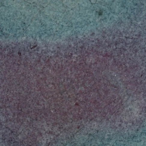 Close-up of a Jun plate, about 3 cm across: a diffuse copper-purple splash spreading into the opalescent pale blue glaze