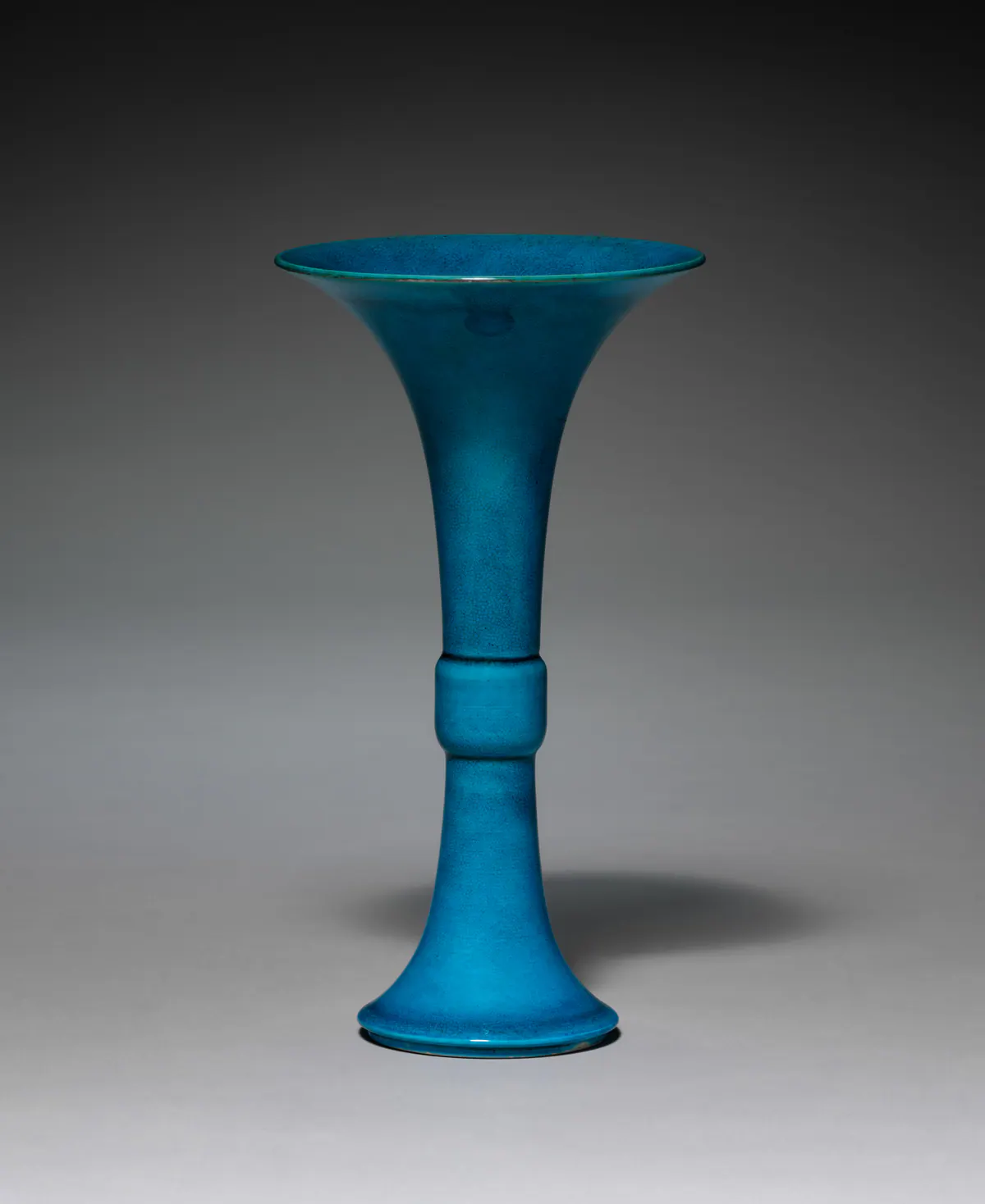 A Kangxi porcelain gu beaker vase in a crackled peacock-blue glaze, with a wide trumpet mouth, a short, slightly swollen band at the middle and a flared foot.