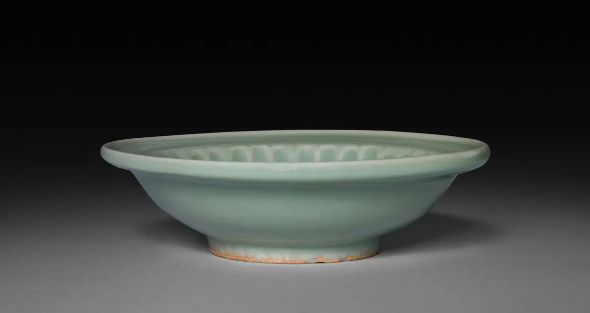 A small Longquan celadon plate on a low foot, with a flat everted rim and moulded petals inside, under a pale blue-green glaze.