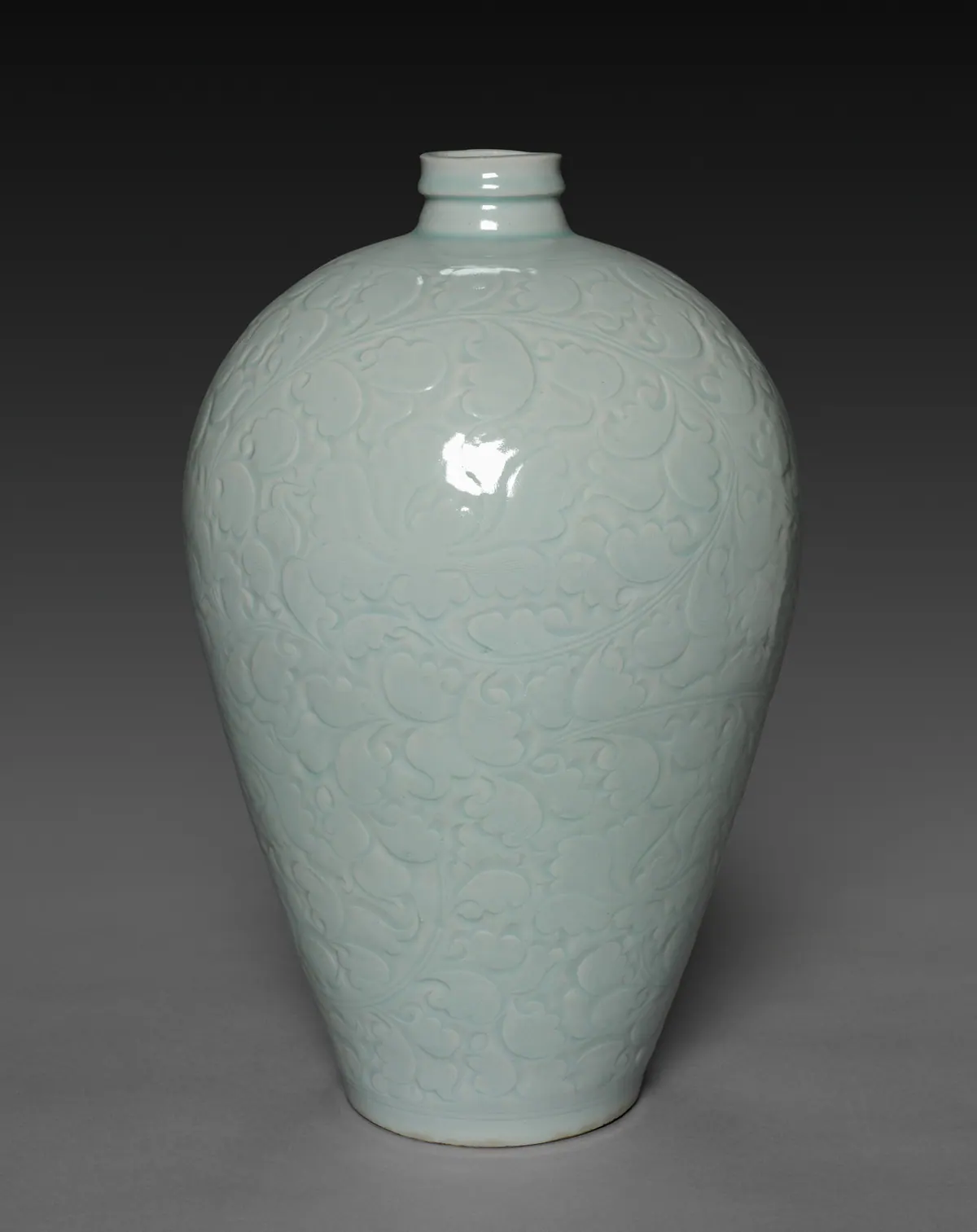 A tall qingbai meiping vase with a narrow neck and broad shoulders, carved all over with scrolling floral sprays, its pale blue glaze deepening in the carved lines.