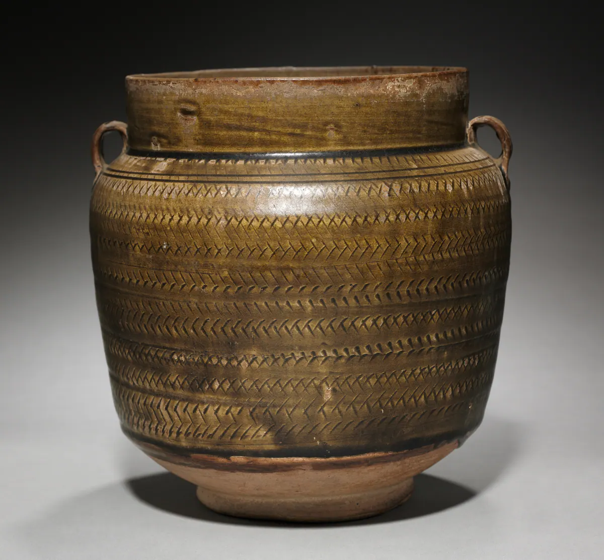 A northern Chinese stoneware jar with two small loop handles, covered in a mottled olive-brown glaze over rows of impressed chevron bands, the foot left bare.