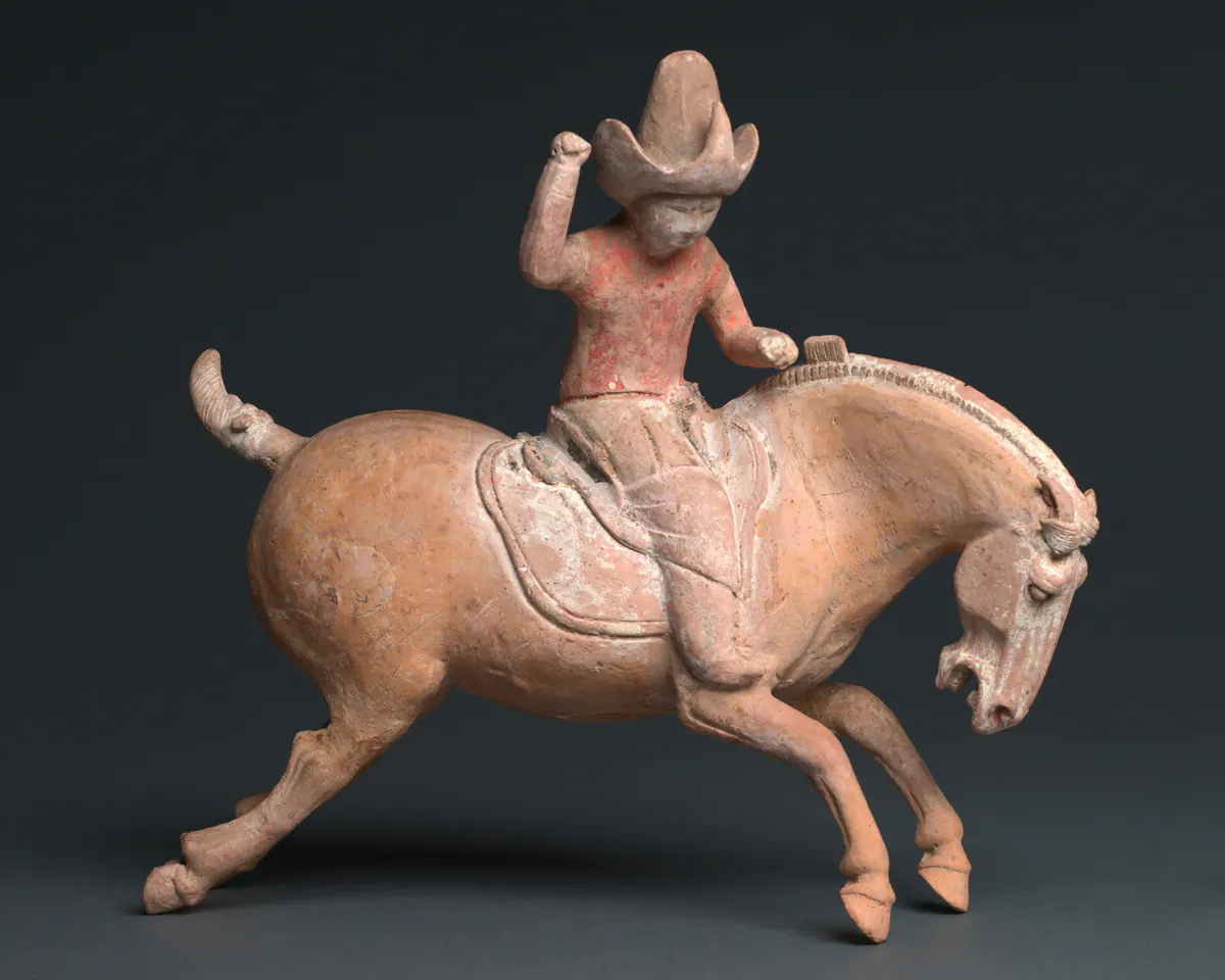 Painted earthenware tomb figure of a polo player in a tall hat on a galloping horse, one fist raised, with traces of red pigment on the rider's tunic.