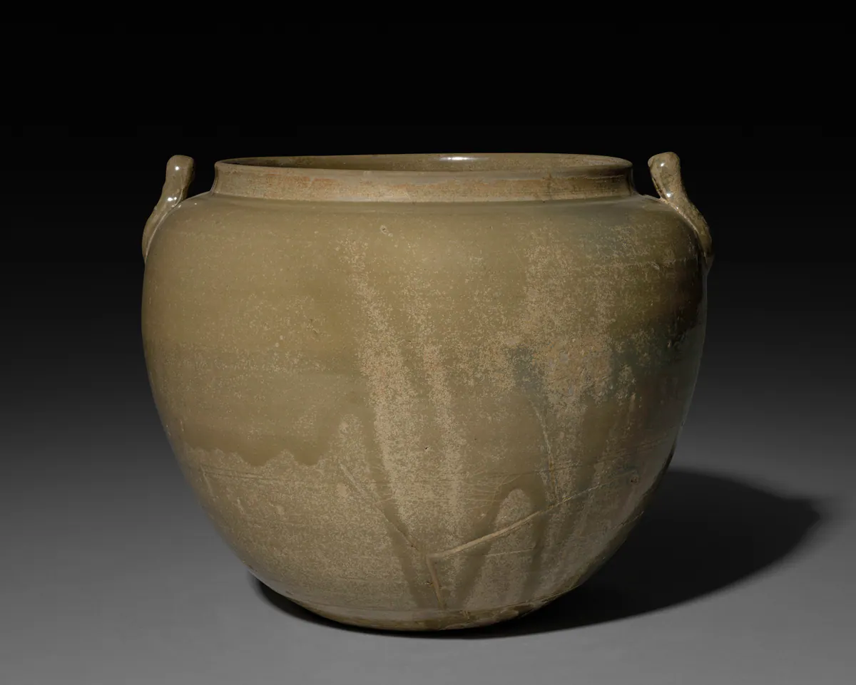A wide-bodied Yue ware stoneware jar with a short neck and small handles on the shoulder, under an even olive-green glaze with paler mottled patches.