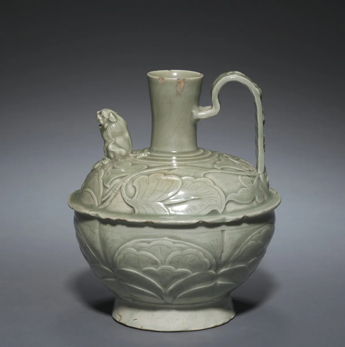A Yaozhou celadon ewer with a tall neck, a high looped handle and a small seated lion forming the spout on the shoulder, its grey-green glaze over deeply carved peony and leaf decoration.
