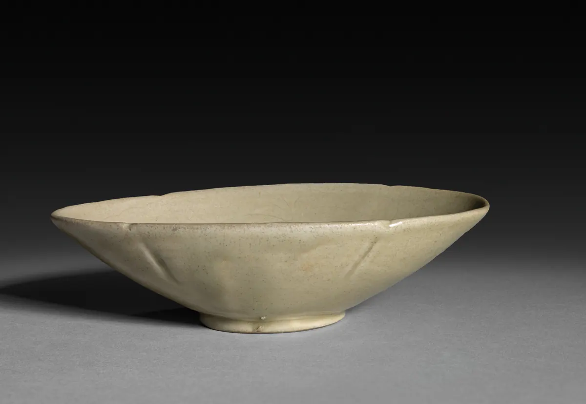 A shallow oval Yue ware cup with a lobed rim and a low foot, under a pale grey-green glaze, with faint incised petals visible inside.