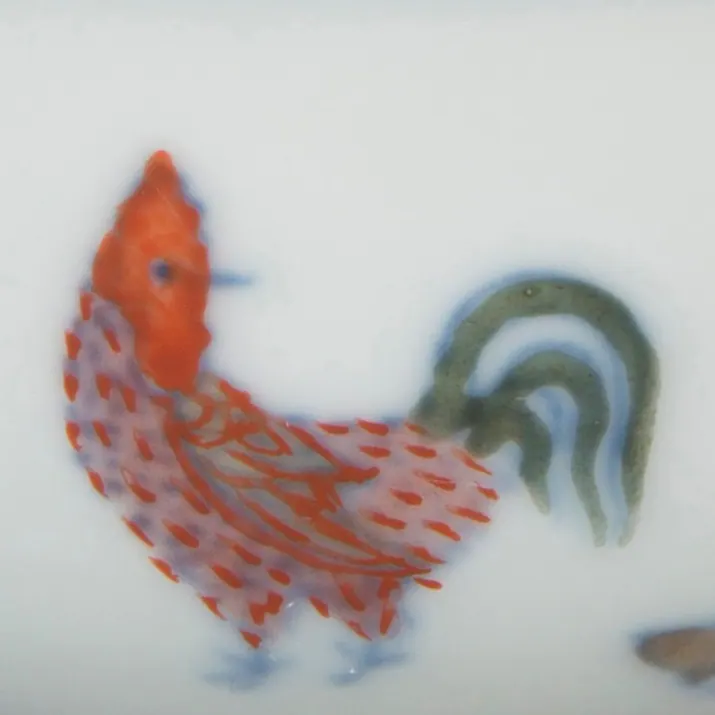 Detail of a Chenghua chicken cup: a rooster drawn in fine underglaze blue outlines and filled with iron-red and green enamels on white porcelain
