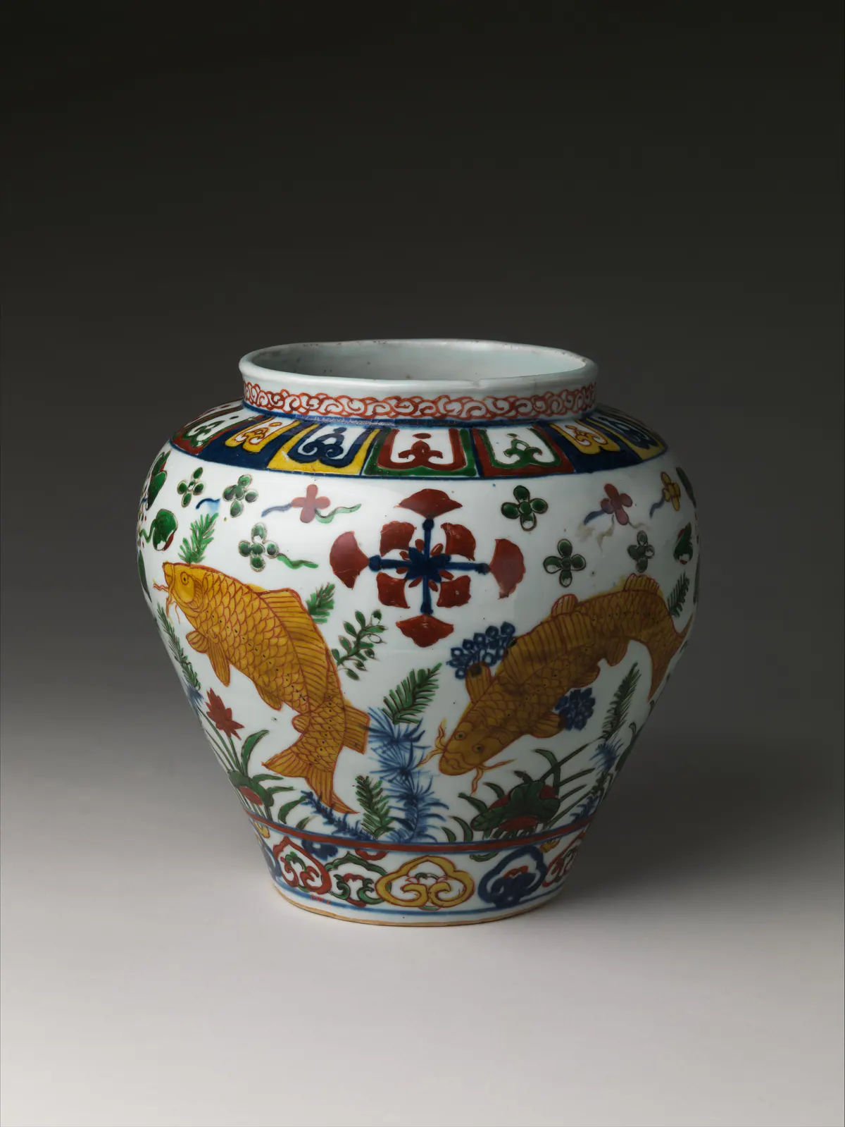 Jiajing mark and period wucai jar painted with golden carp among water plants and lotus, in iron red, green, yellow and underglaze blue, with a band of shaped panels on the shoulder.