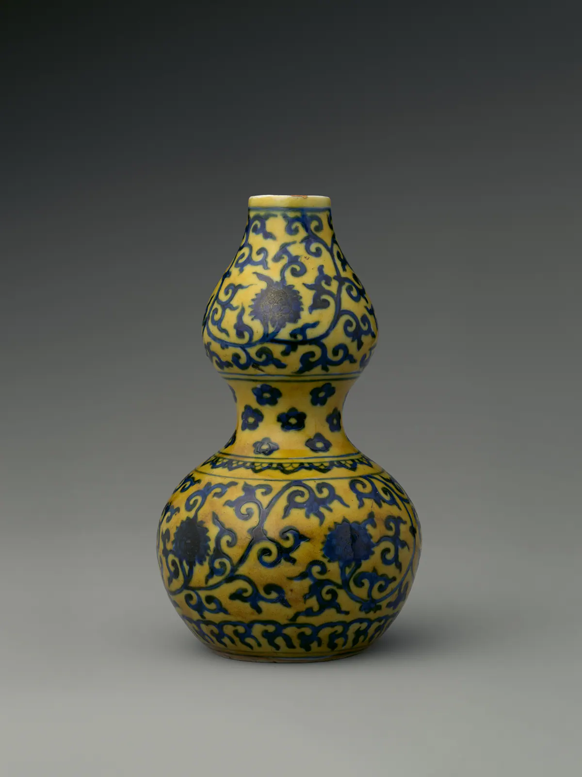 A Jiajing porcelain double gourd bottle, two rounded bulbs joined at a narrow waist, painted in underglaze blue with flower scrolls and small flower heads on a bright yellow ground.