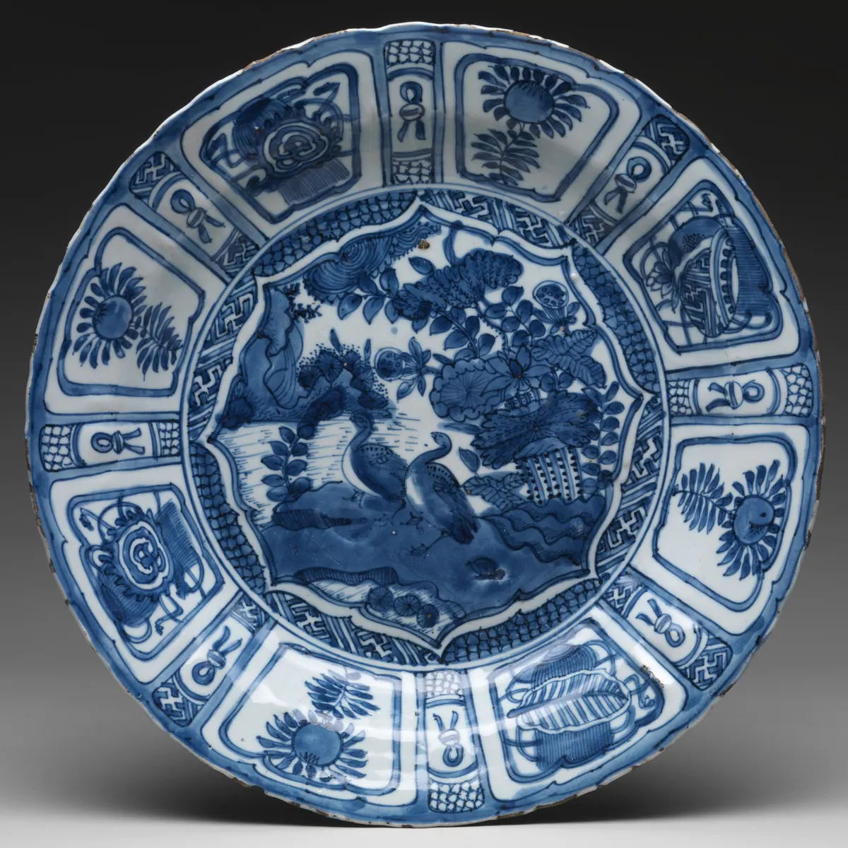 Front of a Wanli period kraak dish, cropped close: geese by a lotus pond in a lobed medallion, ringed by diaper and fret, within a border of wide and narrow panels