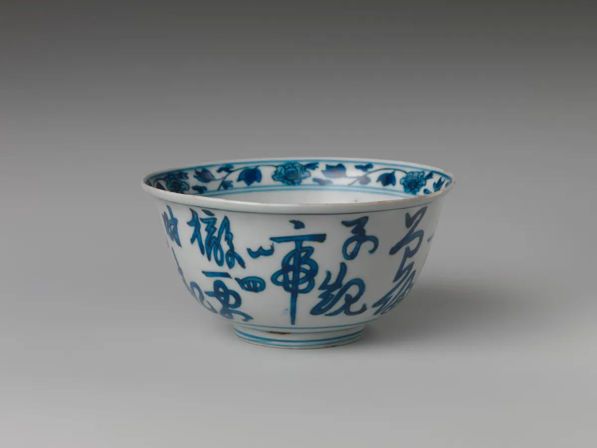 A Longqing blue and white bowl with a flared rim, its outside written with large characters in a flowing cursive script, and a scroll of flowers and leaves inside the rim.