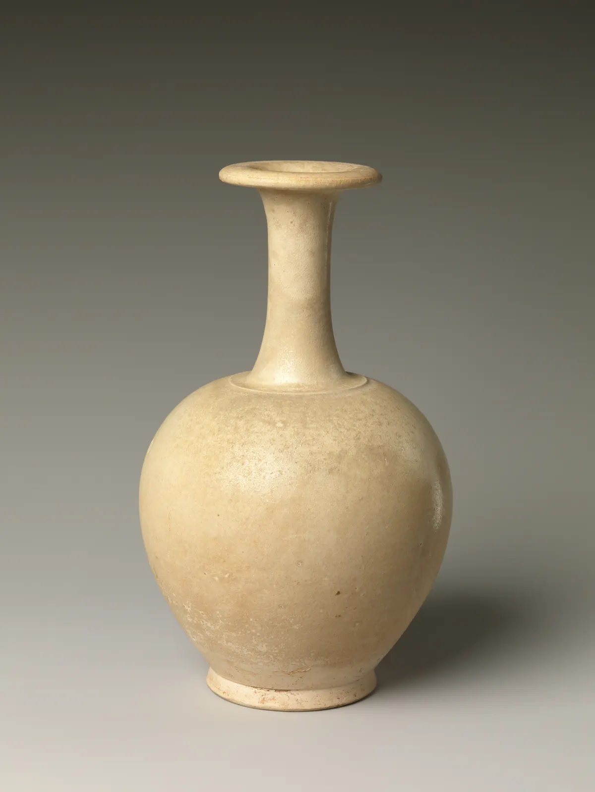 A plain Sui dynasty bottle with a round body, a long narrow neck and a flat dished mouth, its pale body covered in a thin clear glaze that has worn in places.