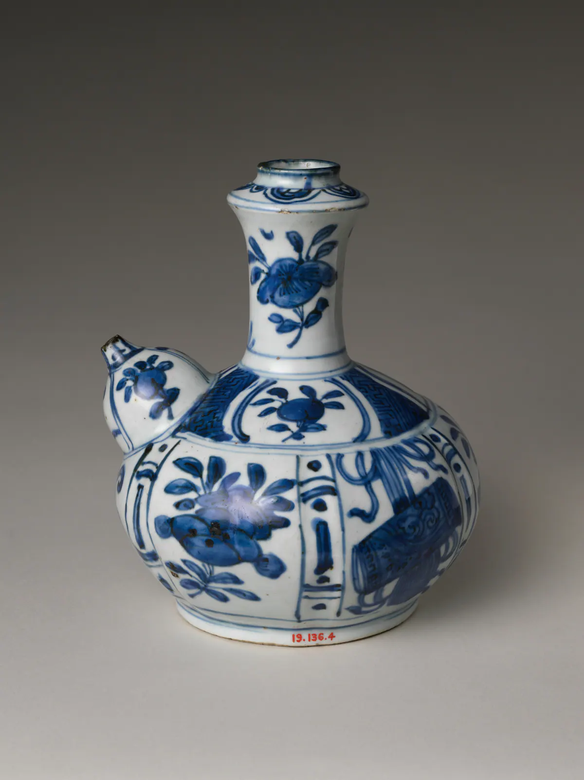 A Wanli blue and white kendi with a round lobed body, a tall upright neck and a bulbous spout on the shoulder, painted in panels with flowers, fruit and scholarly objects.