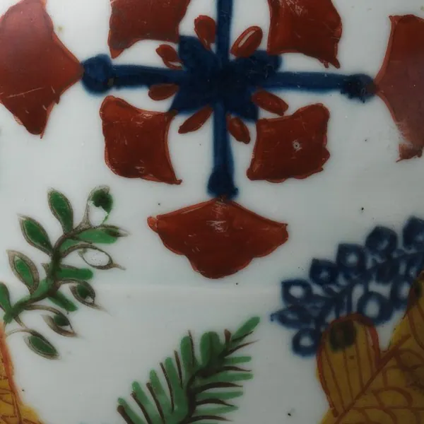 Detail of a Jiajing wucai jar: an underglaze blue cross painted as solid colour among iron-red petals, beside green sprays, a blue water plant and a yellow carp outlined in red