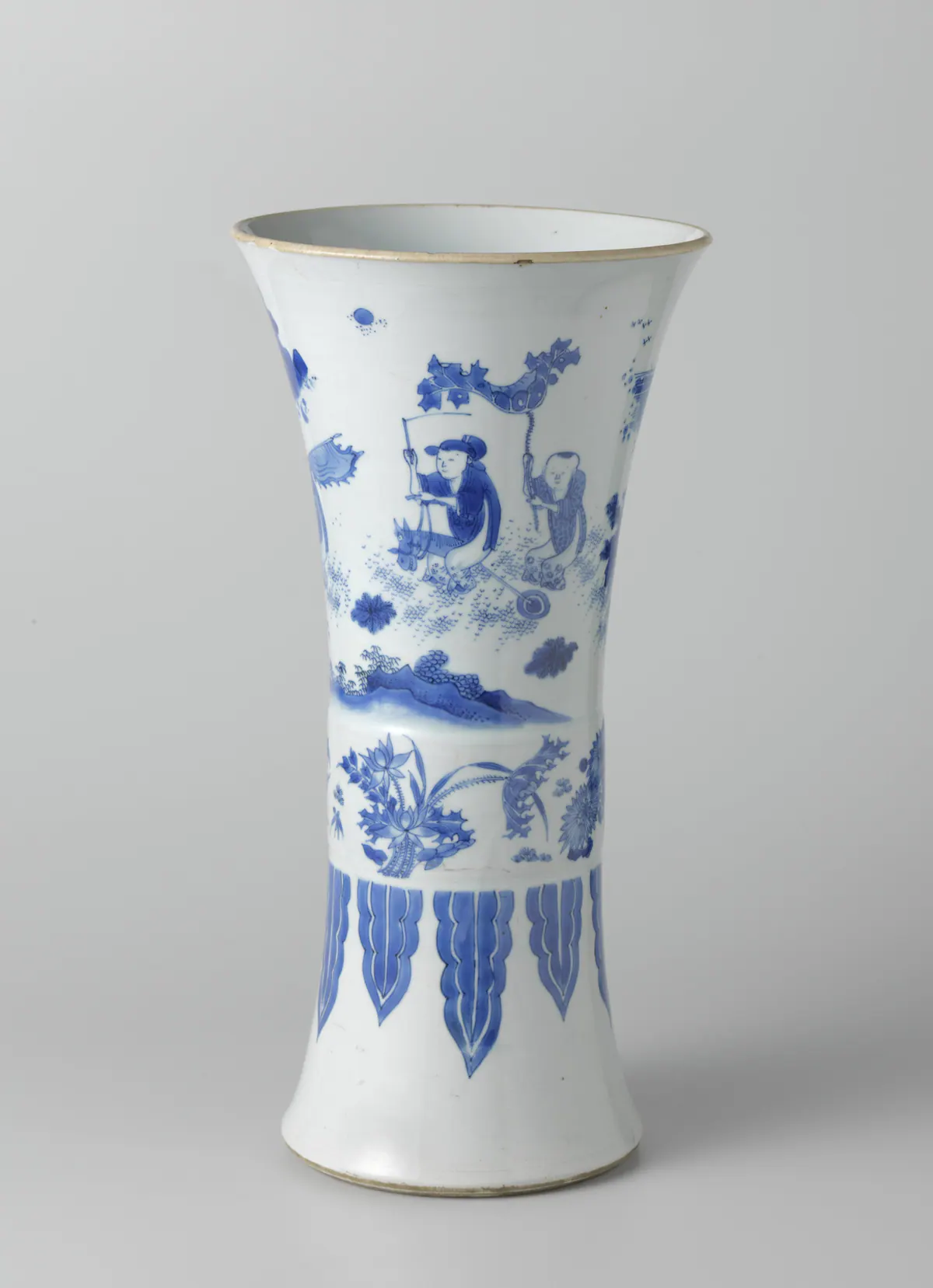 A Transitional blue and white beaker vase with a wide flared mouth, painted with boys playing in a landscape, one on a hobby horse, above a band of flowers and tall stiff leaves.